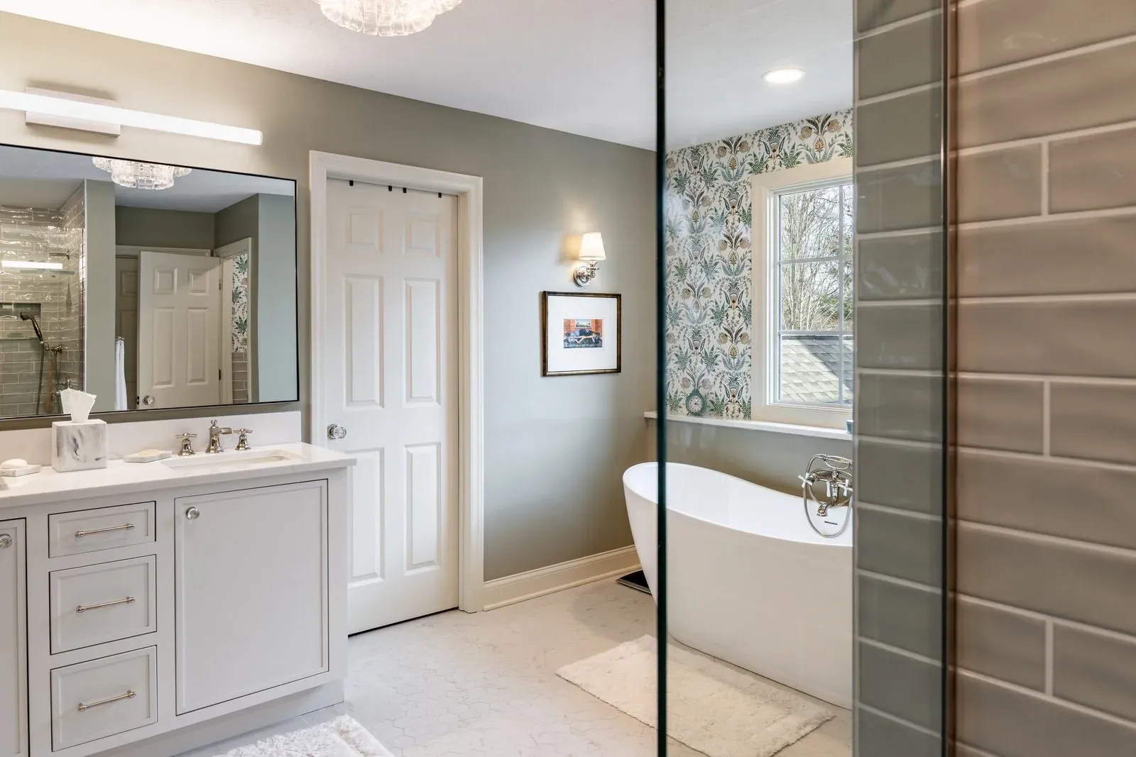 Blacklick bathroom remodel seen past the shower glass, with a white quartz-topped vanity, a freestanding tub and a bronze tile shower wall