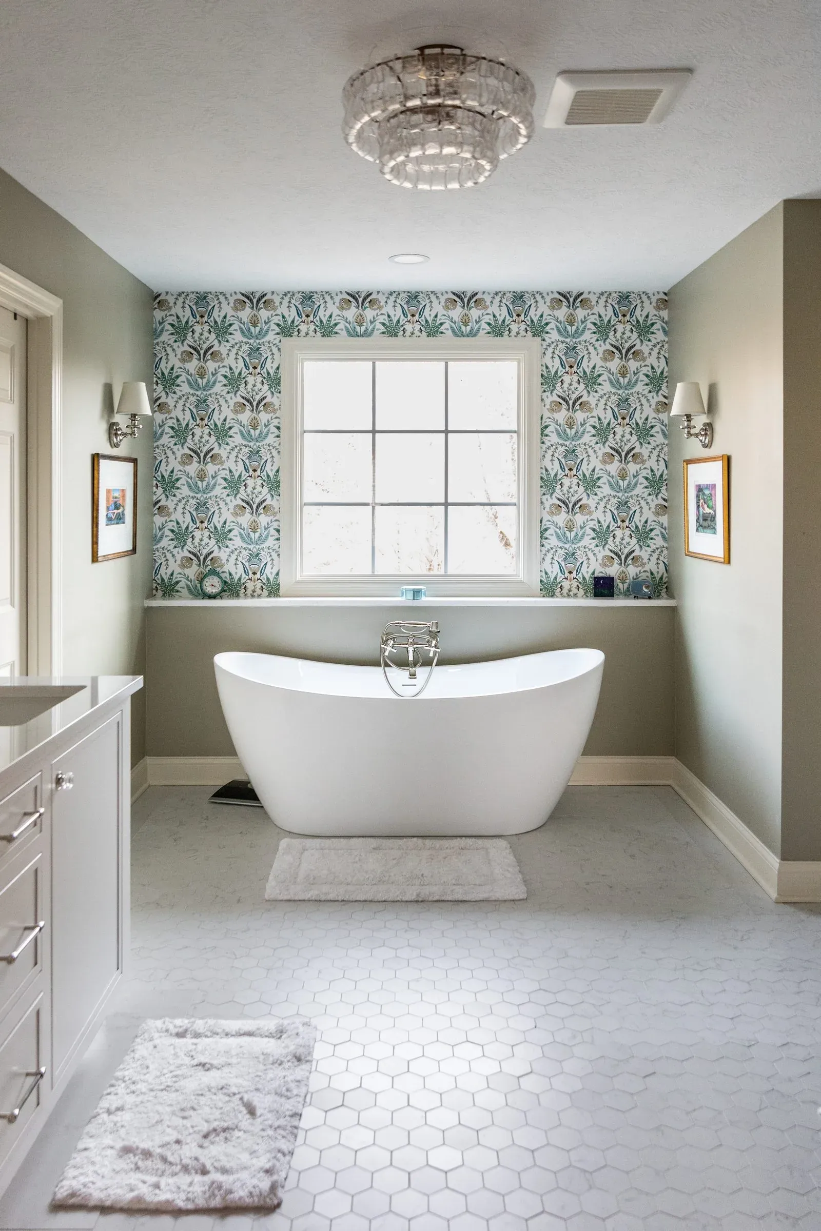 Primary bathroom looking down the room to a freestanding tub under a wallpapered window wall, over a white marble hexagon tile floor