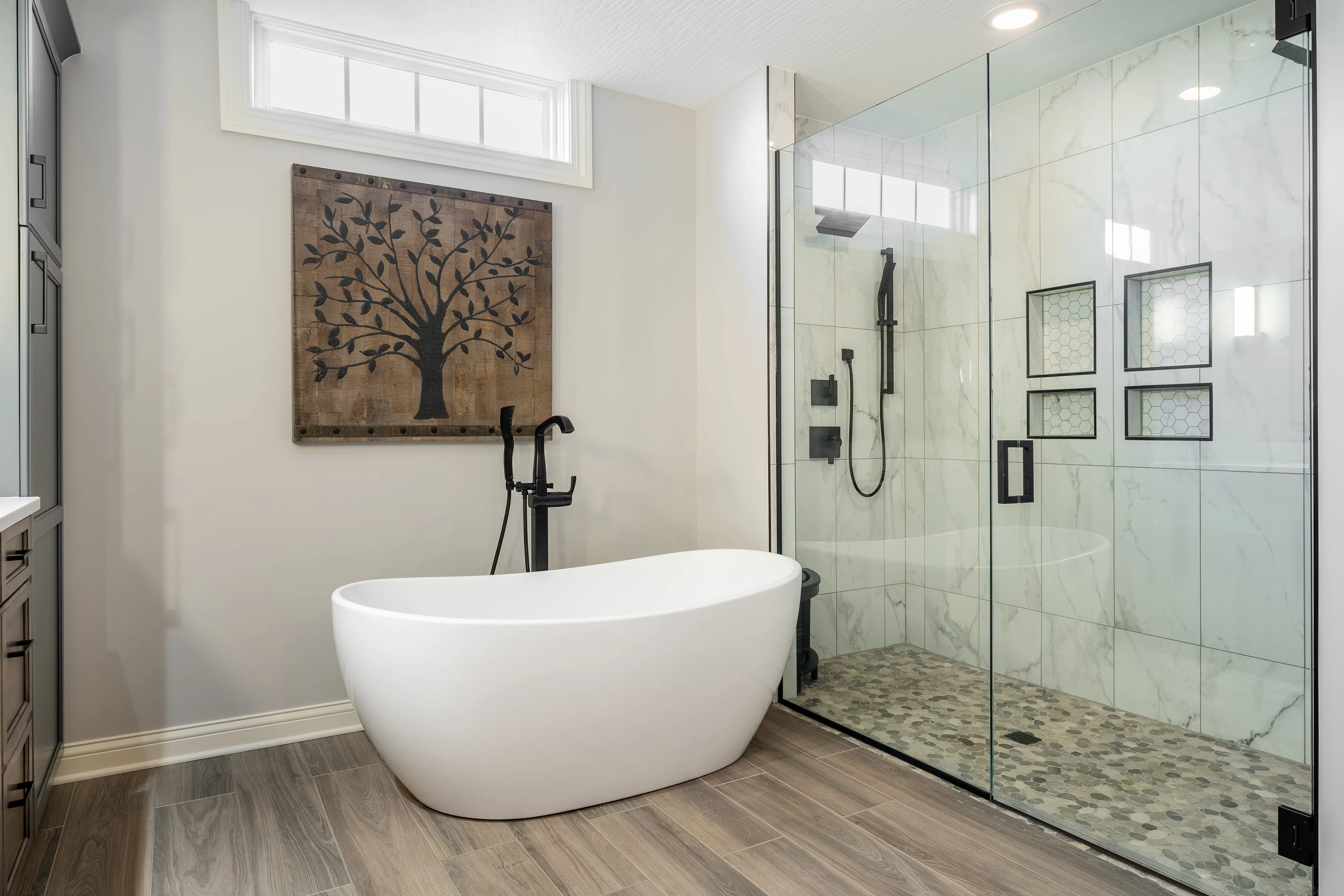 Remodeled Columbus bathroom with a white freestanding soaking tub, matte black floor-mounted tub filler and a frameless glass walk-in shower tiled in marble-look porcelain