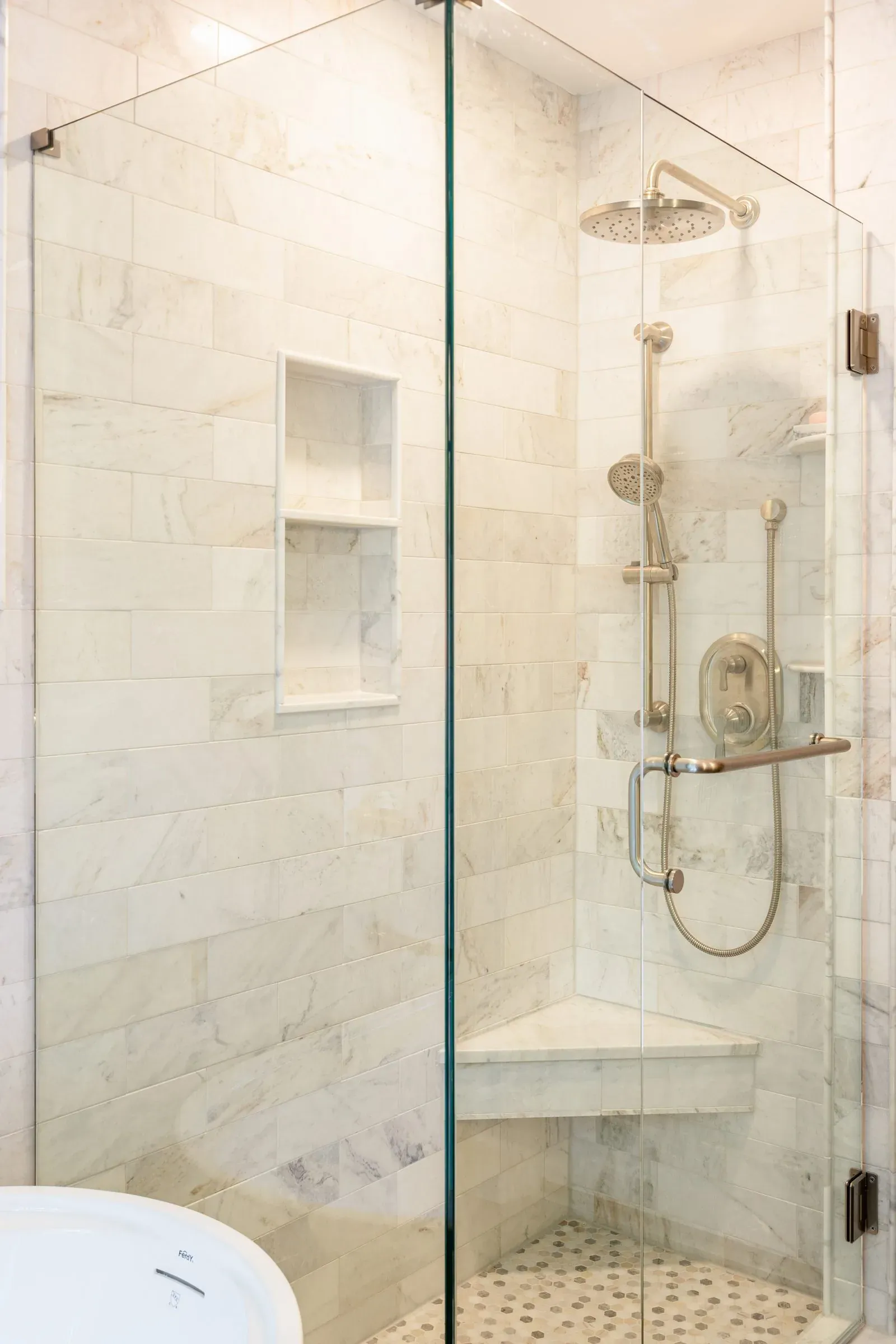 Shower interior tiled in marble subway with a recessed niche, brushed nickel slide bar, rain head and a built-in corner bench
