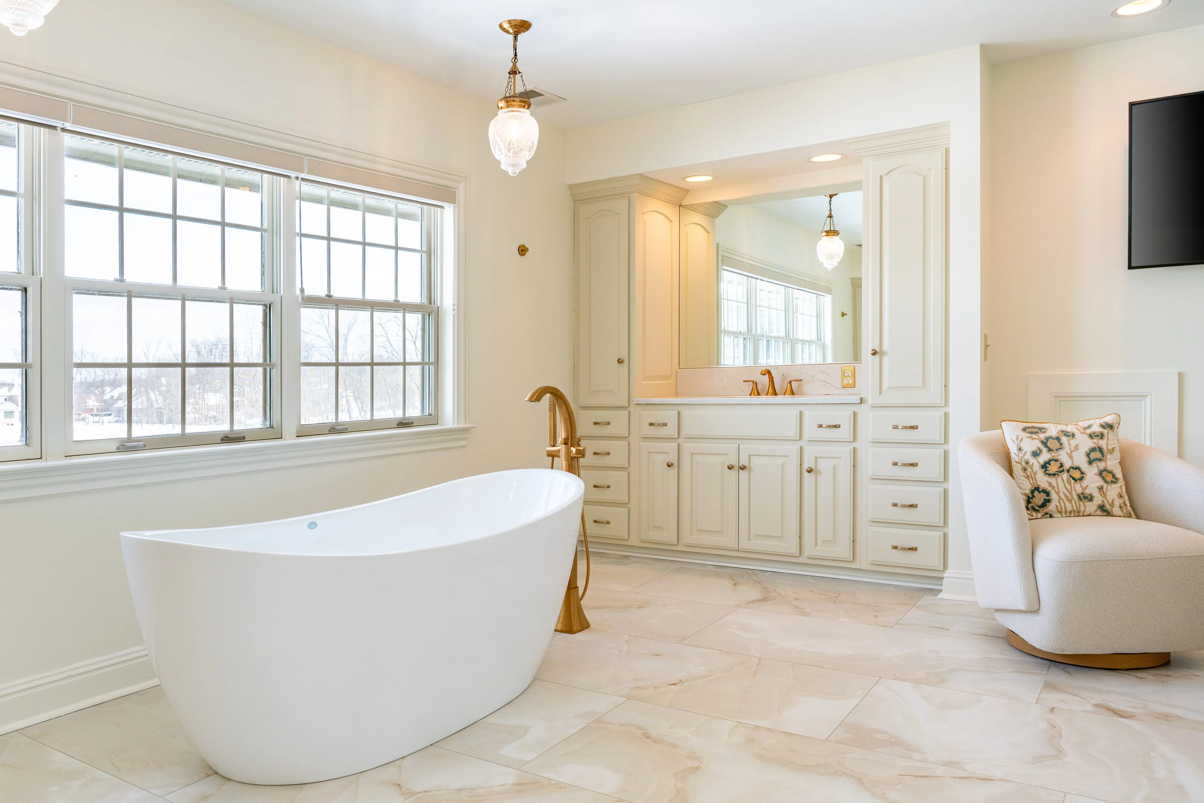 Columbus primary bathroom remodel with a white freestanding soaking tub, a brushed gold floor-mounted tub filler, cream inset vanity cabinetry and a wall of windows