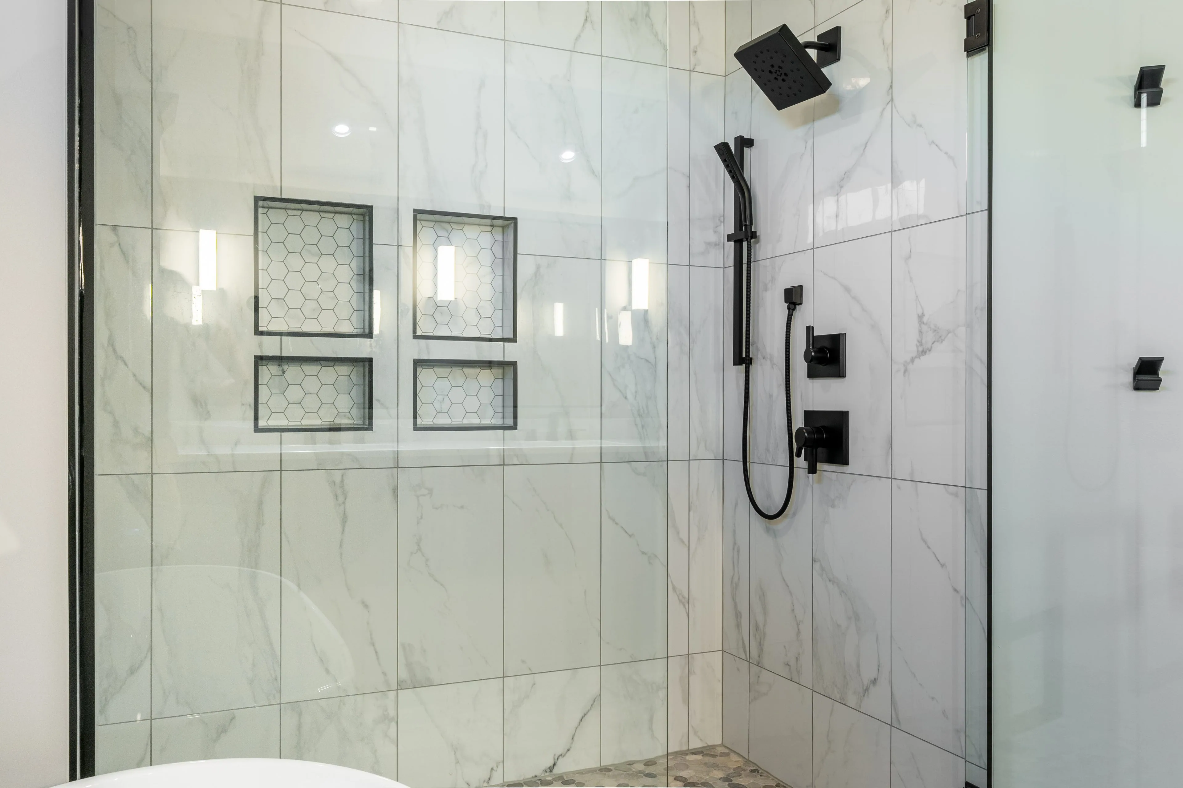 Newly installed walk-in shower in Columbus with large-format marble-look tile, two recessed hexagon-tiled niches, matte black controls and a frameless glass enclosure