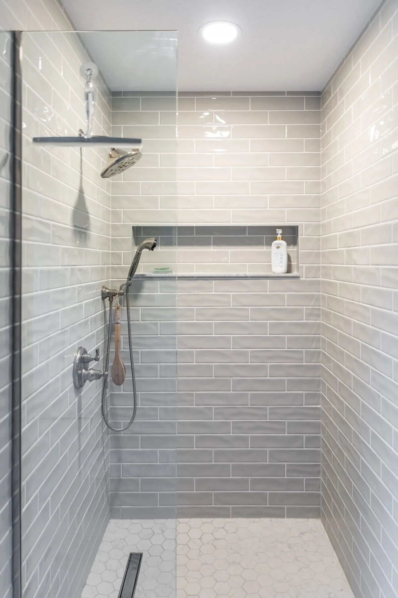 Walk-in shower installed where a tub used to sit, tiled in grey subway with a full-width recessed niche and a polished nickel hand shower