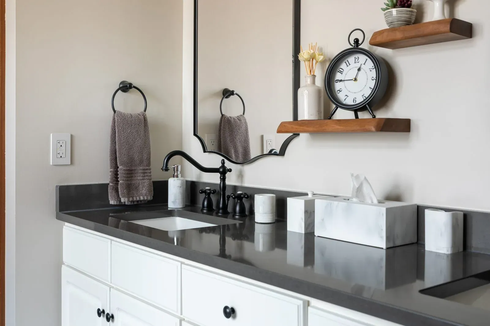 Double vanity in a Westerville bathroom remodel with charcoal quartz countertop, oil-rubbed bronze cross-handle faucets and a walnut display shelf