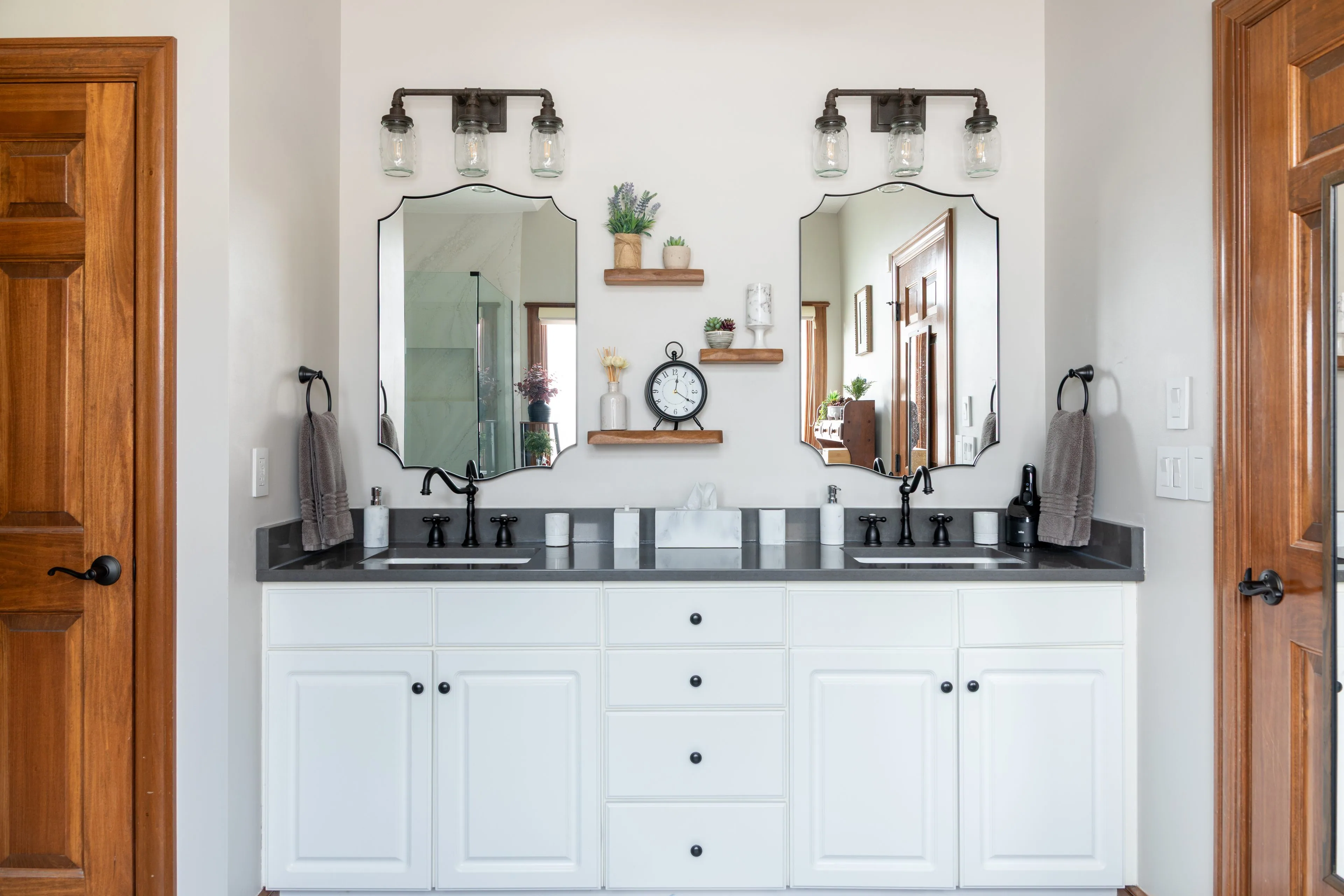 Westerville bathroom remodel with a white double vanity, charcoal quartz countertop, oil-rubbed bronze faucets, arched mirrors and open walnut shelving